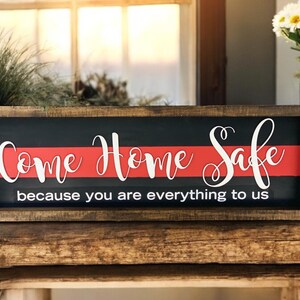 May include: A wooden sign with a red and black background. The sign says "Come Home Safe because you are everything to us".