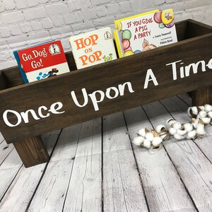May include: A brown wooden book holder with the words "Once Upon A Time" painted in white. The holder has four legs and is filled with children's books, including "Go, Dog, Go!" and "Hop on Pop".