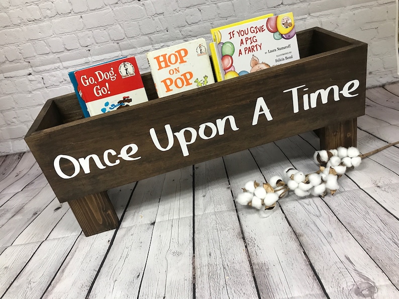 May include: A brown wooden book holder with the words "Once Upon A Time" painted in white. The holder has four legs and is filled with children's books, including "Go, Dog, Go!" and "Hop on Pop".
