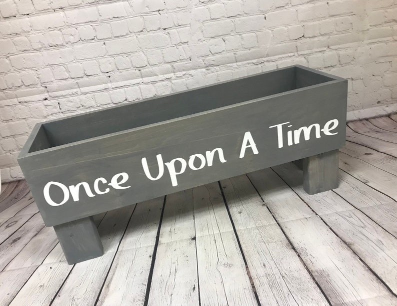 May include: A gray wooden box with the words "Once Upon A Time" written in white paint. The box is sitting on four short legs.