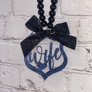 Pu&ograve; includere: Ciondolo per auto in glitter blu con un fiocco nero e la parola "Wife" in corsivo. Il ciondolo &egrave; appeso a una corda di perline nere.