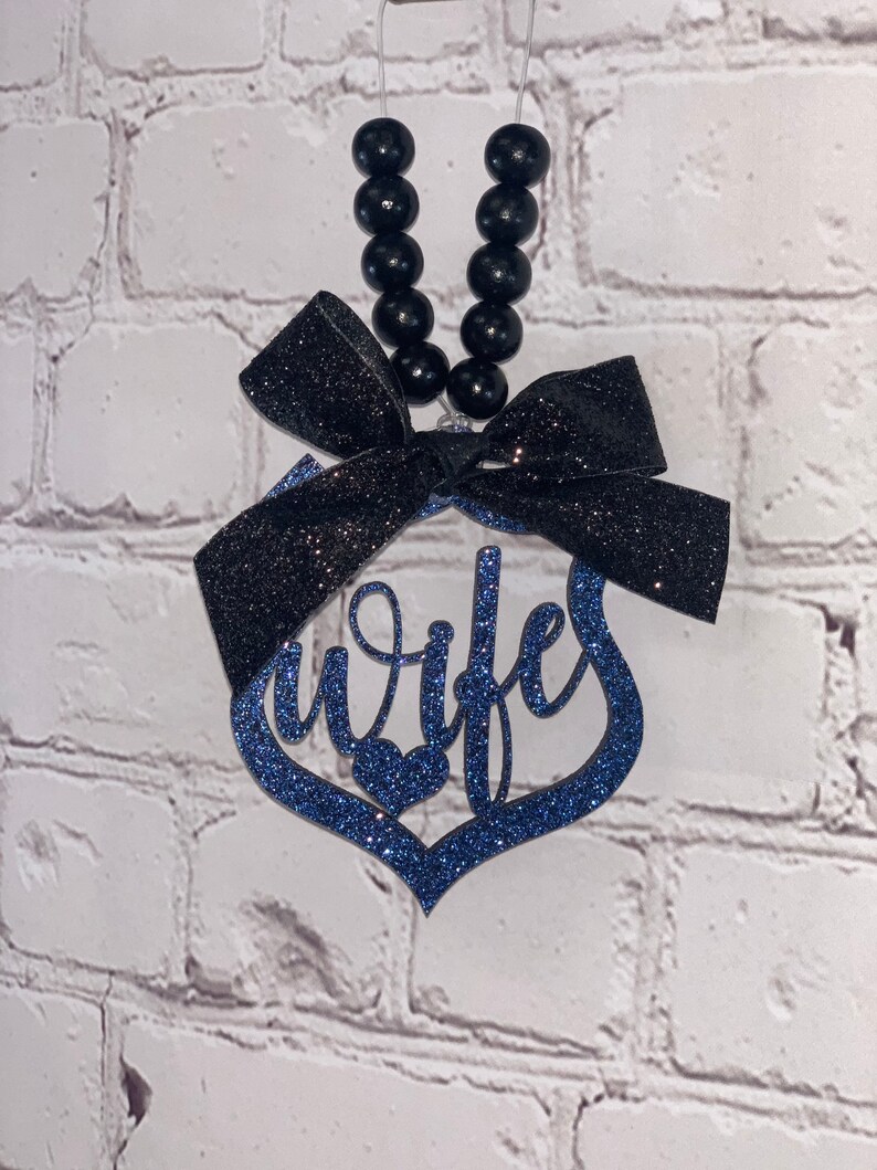 Pu&ograve; includere: Ciondolo per auto in glitter blu con un fiocco nero e la parola "Wife" in corsivo. Il ciondolo &egrave; appeso a una corda di perline nere.
