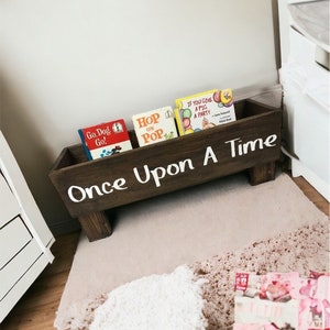 May include: A wooden book bin with the words "Once Upon A Time" painted on the front. The bin is filled with children's books, including "Go Dog Go!" and "Hop on Pop".
