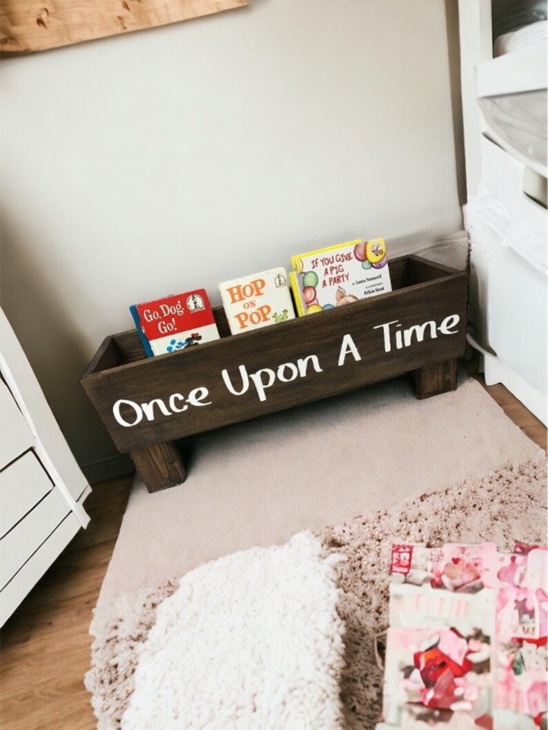 May include: A wooden book bin with the words "Once Upon A Time" painted on the front. The bin is filled with children's books, including "Go Dog Go!" and "Hop on Pop".
