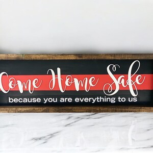 May include: A wooden sign with a red and black background. The sign says "Come Home Safe because you are everything to us".