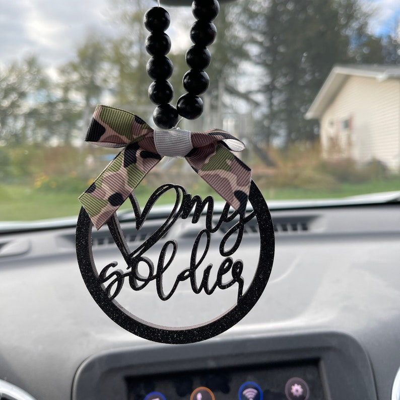 Peut inclure: Noeud en ruban camouflage noir et vert avec un cercle noir paillet&eacute; qui dit "My Soldier" suspendu &agrave; une cha&icirc;ne de perles noires.