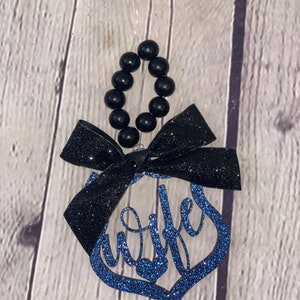Pu&ograve; includere: Ciondolo di glitter blu con la parola "moglie" in corsivo. Il ciondolo ha un fiocco nero e una collana di perline nere per appenderlo.