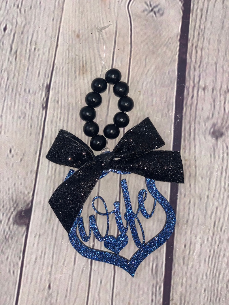 Pu&ograve; includere: Ciondolo di glitter blu con la parola "moglie" in corsivo. Il ciondolo ha un fiocco nero e una collana di perline nere per appenderlo.