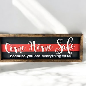 May include: A wooden sign with a black background and a red stripe across the middle. The sign says "Come Home Safe because you are everything to us".