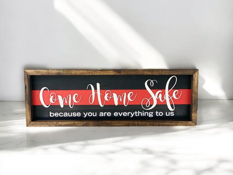 May include: A wooden sign with a black background and a red stripe across the middle. The sign says "Come Home Safe because you are everything to us".
