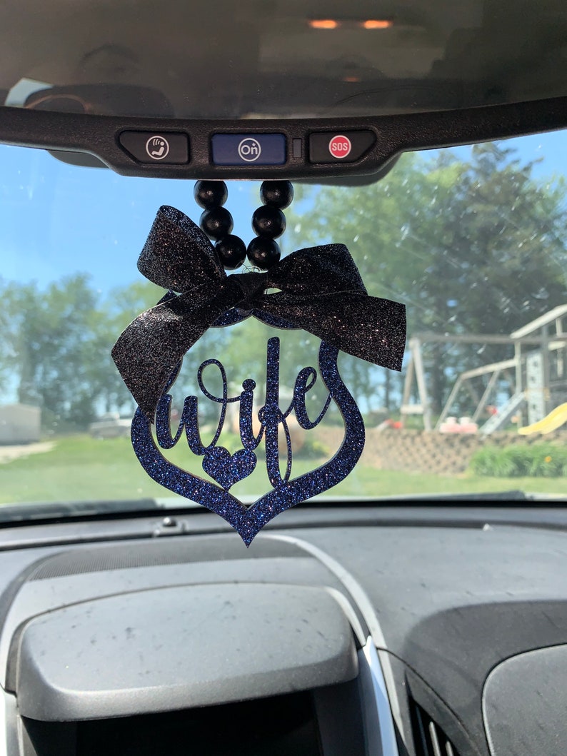 Pu&ograve; includere: Un ciondolo per auto in glitter nero e blu con un cuore e la parola "moglie" appeso allo specchietto retrovisore.
