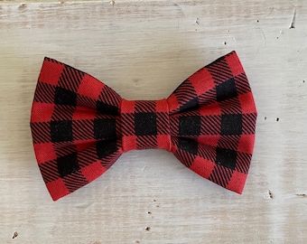 May include: A red and black buffalo plaid bow tie. The bow tie is made of fabric and has a classic shape. The pattern is a bold, checkered design, with large squares of red and black. The bow tie is a stylish accessory.