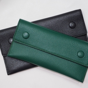 Puede incluir: Dos carteras de cuero, una negra y otra verde, están apiladas una encima de la otra. La cartera verde tiene una solapa con cierre de botón.