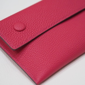 Puede incluir: Una cartera de cuero rosa con cierre de presión.