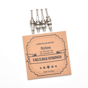May include: Four silver ukulele tuning pegs are positioned above a brown card. The card reads "LONGTEAM MUSIC Nylon UKULELE STRINGS" with string gauges listed. The text "Made in China" is at the bottom.