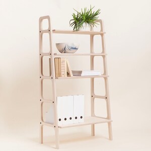 May include: A light wood bookshelf with four shelves and a plant on the top shelf. The shelves are filled with books, folders, and a bowl.