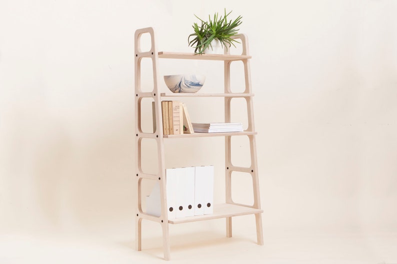 May include: A light wood bookshelf with four shelves and a plant on the top shelf. The shelves are filled with books, folders, and a bowl.