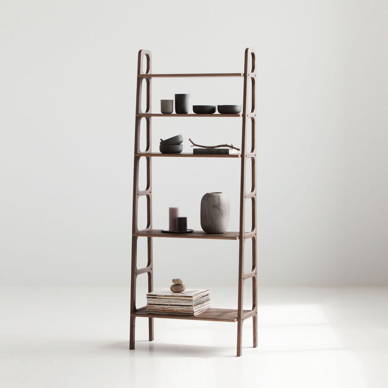 Op de afbeelding: Een houten boekenkast met vijf planken. De planken zijn gevuld met verschillende items, waaronder boeken, vazen en decoratieve objecten. De boekenkast is gemaakt van donker hout en heeft een eenvoudig, modern ontwerp.