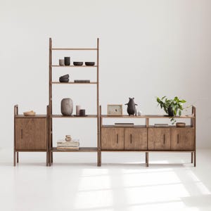 Peut inclure: Un système d'étagères modulable en bois composé d'une unité verticale haute avec des étagères ouvertes et de deux meubles bas avec portes. Le mobilier en bois sombre présente divers objets décoratifs, dont des bols, un vase, des livres et une plante.