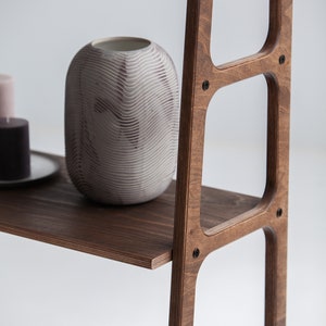 Op de afbeelding: Een houten plankeneenheid met vier planken. De planken zijn gemaakt van donkerbruin hout en hebben een afgeronde rand. De plankeneenheid staat op een wit oppervlak. Een witte keramische vaas met een textuurontwerp staat op de bovenste plank.