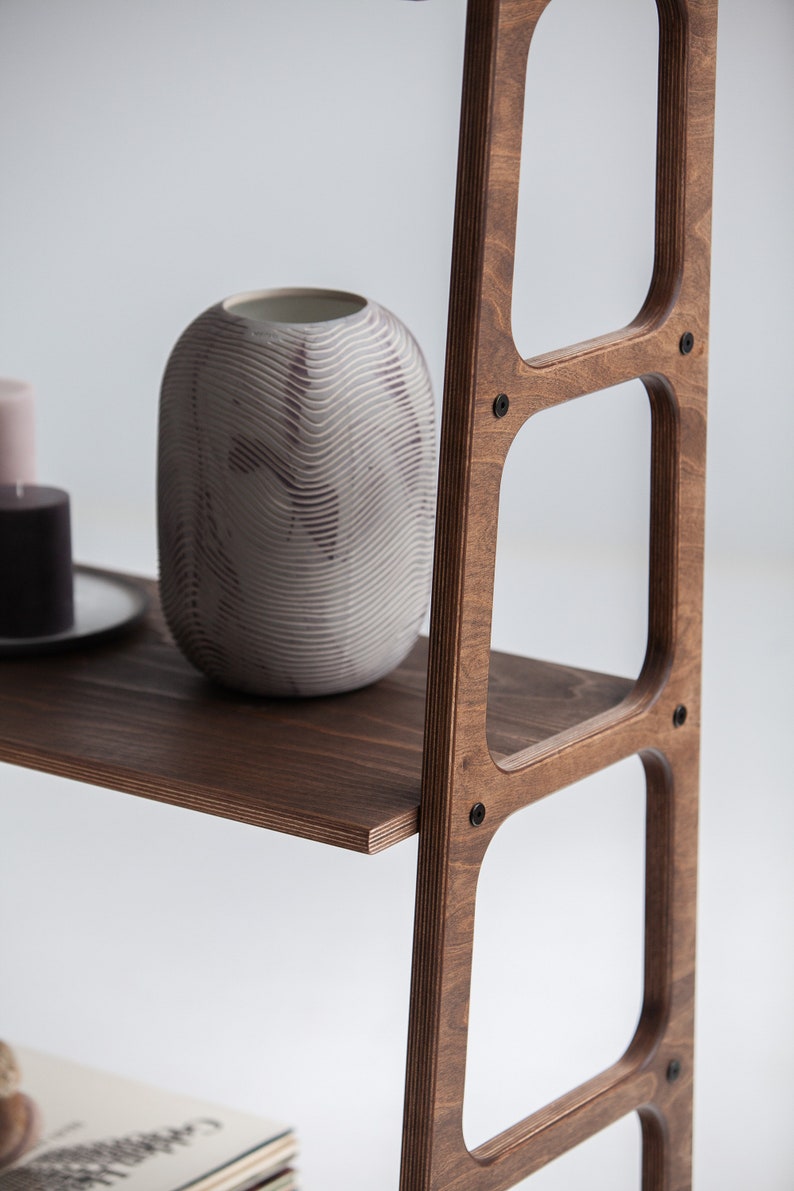 Op de afbeelding: Een houten plankeneenheid met vier planken. De planken zijn gemaakt van donkerbruin hout en hebben een afgeronde rand. De plankeneenheid staat op een wit oppervlak. Een witte keramische vaas met een textuurontwerp staat op de bovenste plank.