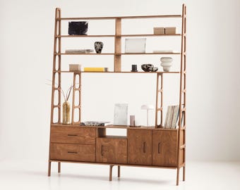 May include: A wooden bookshelf and cabinet unit with open shelves and closed cabinets. The unit has a light brown wood finish and features a variety of decorative items, including vases, books, and artwork.