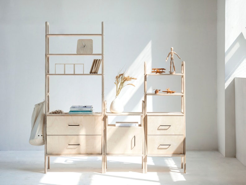 May include: A set of modular wooden shelves with drawers and open shelves. The shelves are made of light wood and have a simple, modern design. The shelves are arranged in a staggered pattern, creating a unique and interesting look.