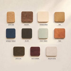 May include: A collection of eleven square wooden swatches arranged in three rows, featuring various finishes labeled as Light Oak, Walnut, Transparent, Oak, Midnight Indigo, Black, Frost Green, Teak, Antic Oak, Rusty Brown, and Frozen White.