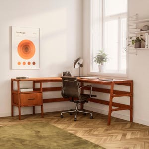 May include: A corner desk with a wooden frame and shelves. The desk has a light brown finish and a black office chair. A framed print with the text "bauhaus 1919" is hanging on the wall.
