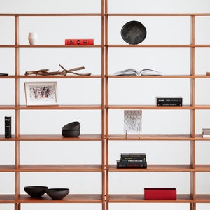 Close-up of the wide mid century modern wooden bookcase showing modular shelves with books and decor, ladder-style side legs and smooth rounded edges in a light oak finish.
