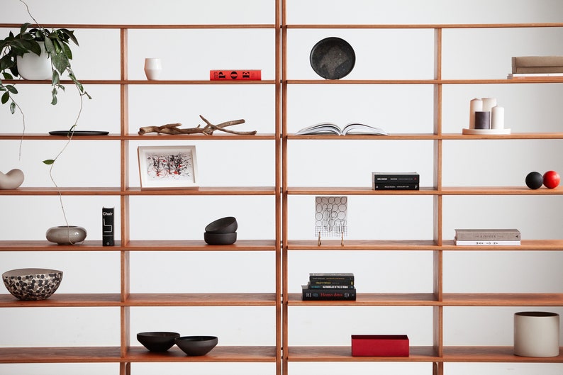 Close-up of the wide mid century modern wooden bookcase showing modular shelves with books and decor, ladder-style side legs and smooth rounded edges in a light oak finish.