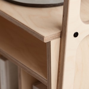 May include: A close-up of a light wood bookshelf with multiple shelves. The shelves are made of plywood and have a natural wood finish. The bookshelf is empty except for a few books on the bottom shelf.