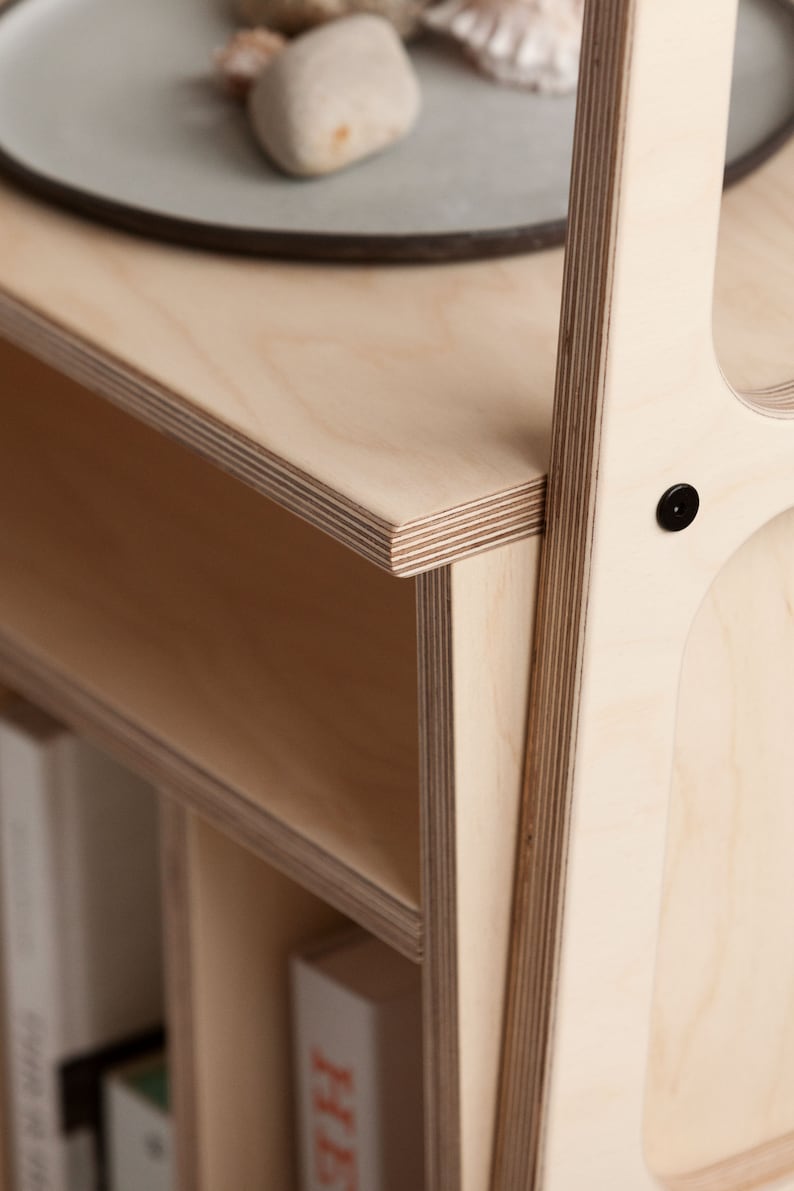 May include: A close-up of a light wood bookshelf with multiple shelves. The shelves are made of plywood and have a natural wood finish. The bookshelf is empty except for a few books on the bottom shelf.