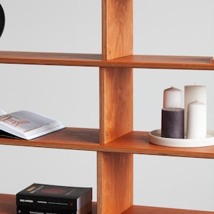 Wide modular wooden bookcase filled with books, bowls, framed art and a plant, used as a living room shelving unit in mid century modern style.