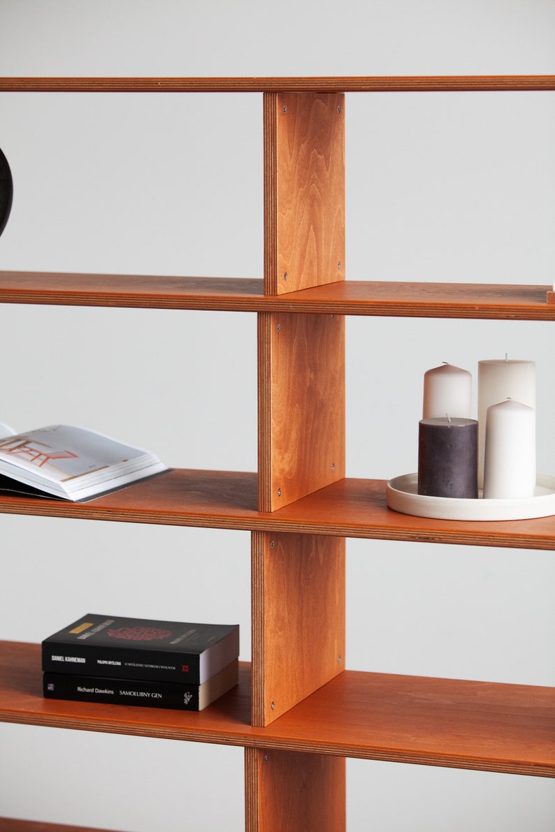 Detail of a handmade wooden bookshelf shelf with an open magazine and stacked books, showing the thin Finnish birch plywood profile and natural wood grain.