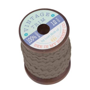 May include: A spool of 12 yards of brown vintage trim with a zig-zag pattern. The spool is labeled "Vintage Trim 100% Cotton by Lori Holt of Bee in My Bonnet Co."