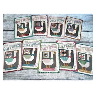 May include: A collection of quilt seed packets featuring a goose design with a bow tie and a quilt block. The packets are in various colors, including green, red, and blue, with the text "QUILT SEEDS".