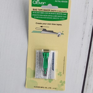 May include: Green bias tape maker tool packaged on a yellow and green card. The card reads "Bias Tape Maker [Width: 6 mm (1/4"])" and "Create your own bias tapes".