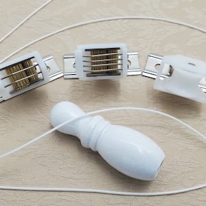 May include: Three white plastic window blind components with metal brackets and a white wooden pull cord. The components are for raising and lowering window blinds.