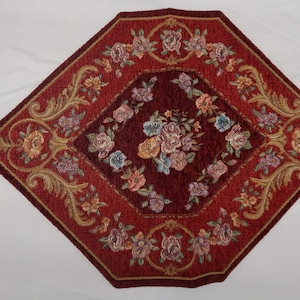 May include: A red and gold diamond-shaped table runner with floral embroidery and tassels on each end.