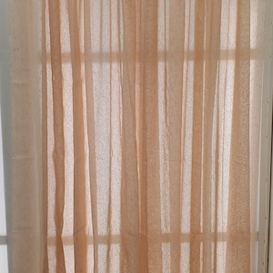 May include: A pair of sheer peach-colored curtains with a ruffled top. The curtains are hanging from a rod and are covering a window.