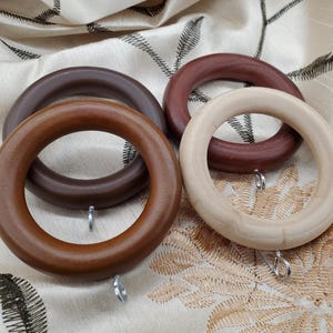 May include: Four wooden curtain rings in different shades of brown. The rings are made of natural wood and have a smooth finish. They are designed to be used with curtain rods.