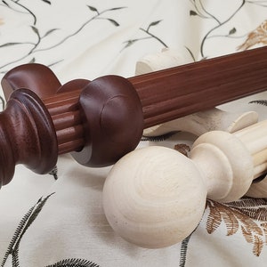 May include: Two wooden curtain rods with decorative finials. One rod is dark brown with a fluted design, and the other is natural wood. The finials are a matching dark brown and natural wood, with a round or ball shape.