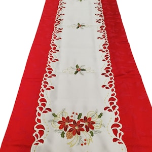 May include: White table runner with a scalloped edge and embroidered poinsettia and holly designs. The runner is on a red background.