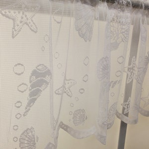 May include: White sheer curtain with a scalloped bottom edge. The curtain features a repeating pattern of seashells, starfish, and bubbles.