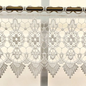 May include: White lace valance with a scalloped bottom edge. The valance has a delicate floral pattern and is perfect for adding a touch of elegance to any window.