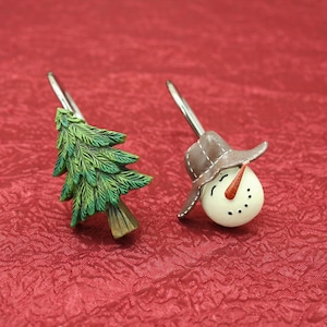 May include: Two decorative shower curtain hooks, one with a green pine tree design and the other with a white snowman design. The hooks are made of metal and have a silver finish.