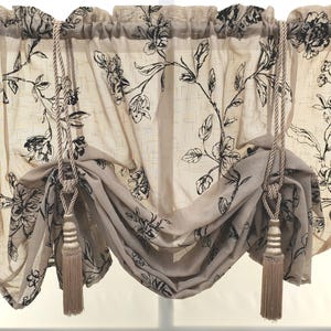 May include: A pair of beige sheer curtains with a black floral pattern and tassel tiebacks.