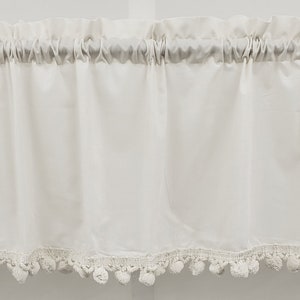 May include: White valance with a white pom-pom trim. The valance is made of a soft, lightweight fabric and has a gathered look.