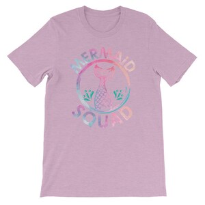 May include: A light purple t-shirt with a watercolor-style graphic of a mermaid tail inside a circle with the text "Mermaid Squad".